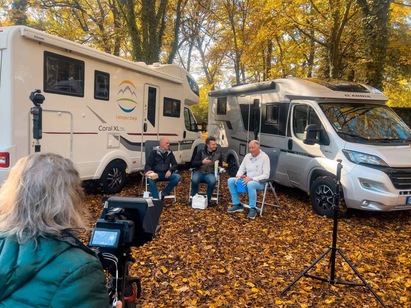 3-blickwinkel-drehtag-fachsimpelrunde Roland, Flo und Frank sitzen vor zwei Wohnmobilen im Herbstlaub, vorne die Kamera von SamPlay