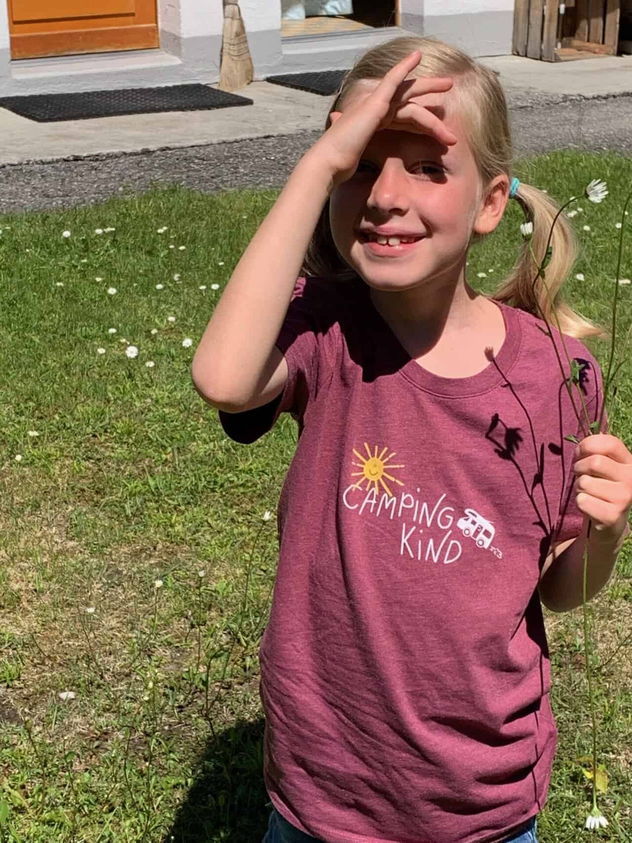 Mädchen im roten T-Shirt mit dem Motiv Camping Kind und kleinem Wohnmobil