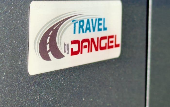 Aufkleber Travel by Dangel mit stilisierter Straße auf der grauen Karosserie des Campers