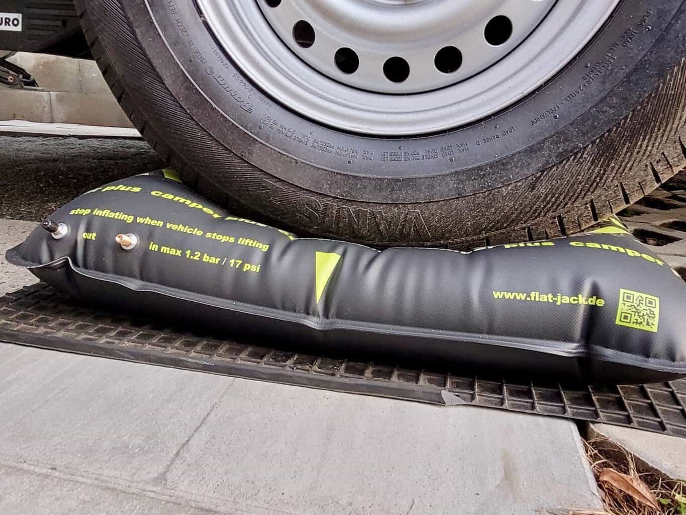 Prall aufgepumptes schwarzes Flat-Jack-Kissen mit gelber Schrift unter dem Reifen eines Wohnwagens, am Kissen zwei Ventile und der Aufdruck „in max 1.2 bar / 17 psi“