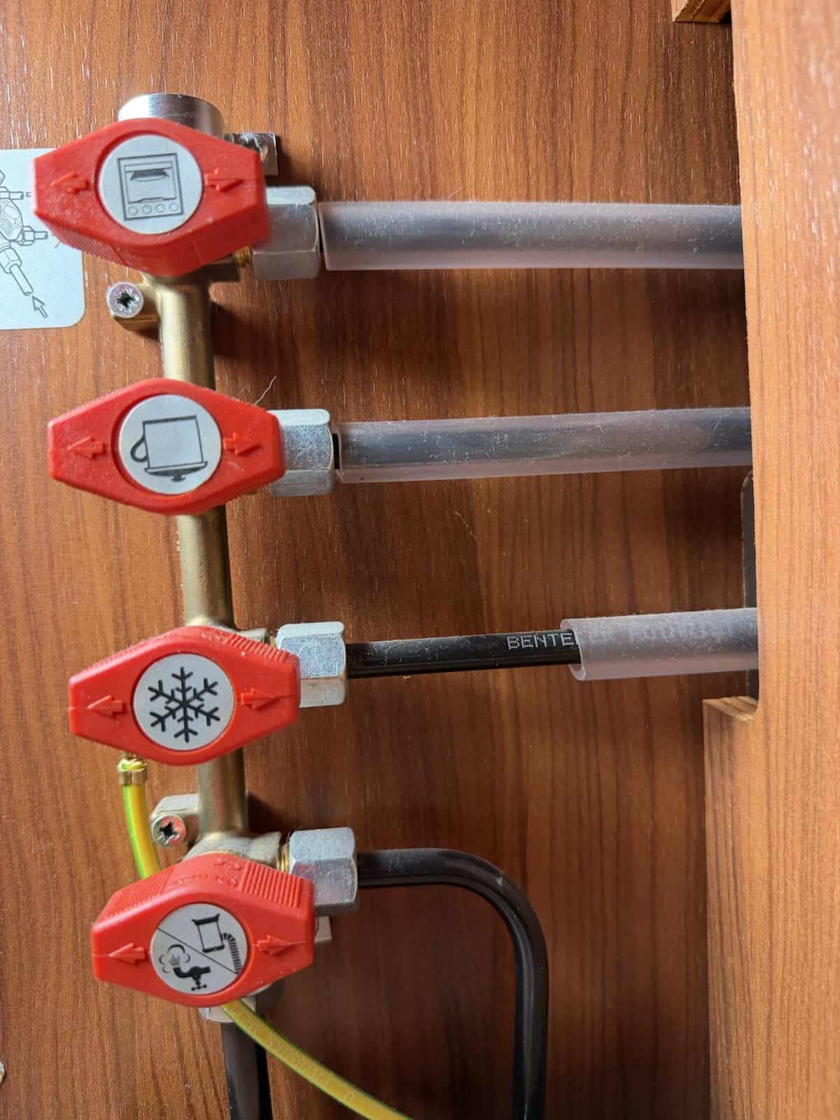 Rote Gas-Absperrhähne im Wohnmobil mit Symbolen für Backofen, Kocher, Kühlschrank und Heizung
