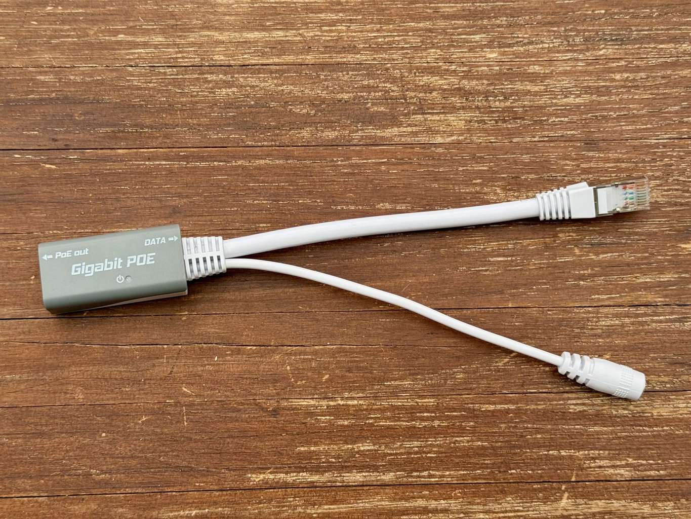 Grauer Adapter mit der Aufschrift Gigabit POE, links ein weißes Netzwerkkabel, rechts eine weiße Buchse für den Hohlstecker