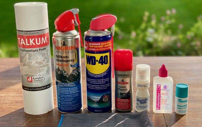 Sieben Pflegemittel für Gummidichtungen auf einem Holztisch: Talkum, Nigrin Silikon-Gleitspray, WD-40, Stifte und Fläschchen