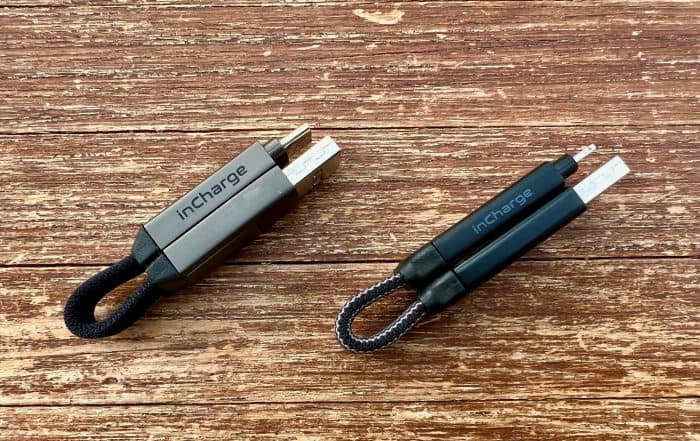 Zwei kurze inCharge-Ladekabel mit Schlaufe auf verwittertem Holz, links das metallfarbene, rechts das dunkle, beide mit mehreren Steckern
