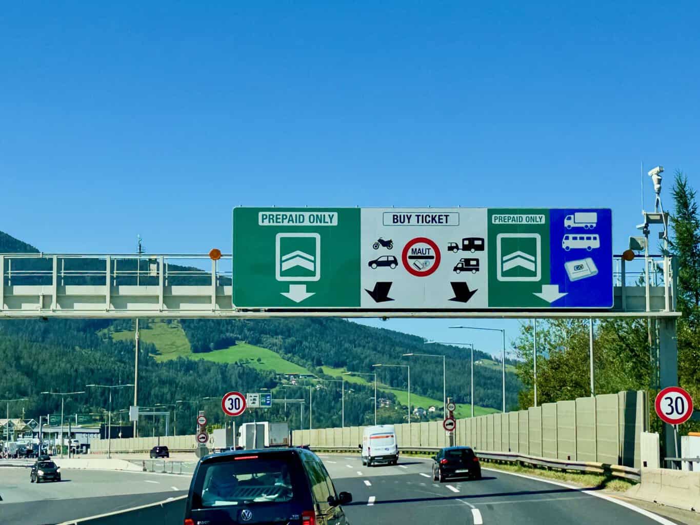 Mautstation mit mehreren Spuren unter blauen Dächern an einer Autobahn im Abendlicht