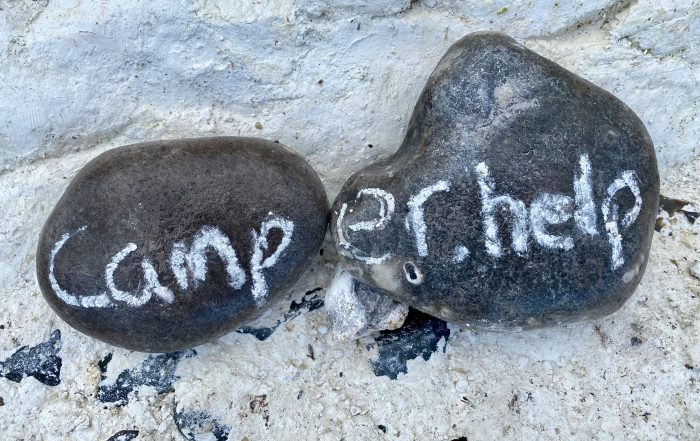 Zwei dunkle Kieselsteine auf hellem Fels, mit Kreide camper.help darauf geschrieben