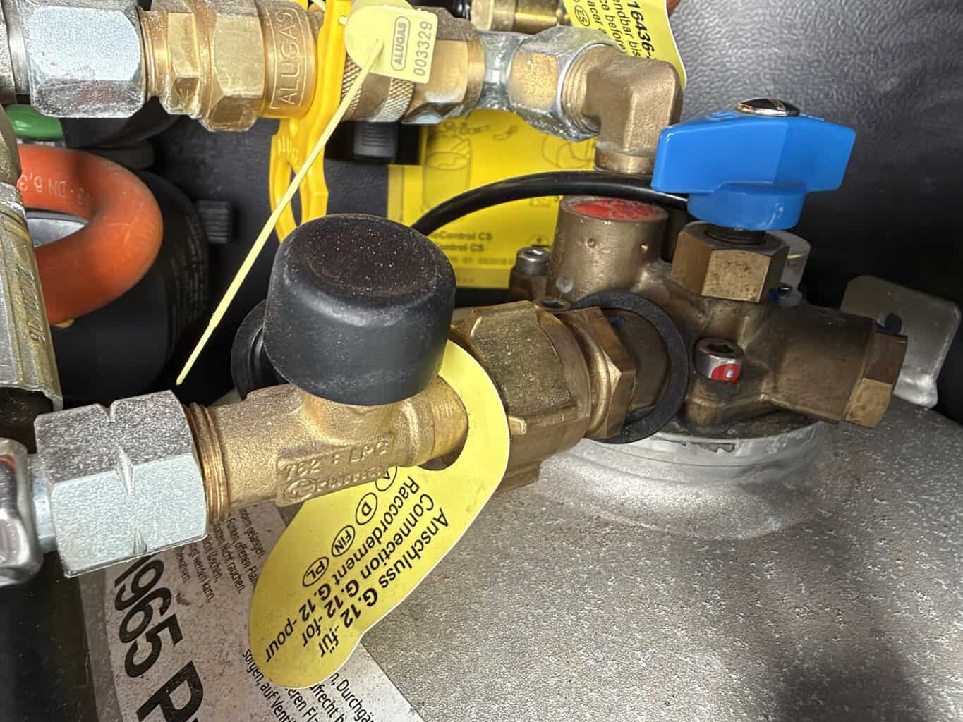 Truma Schlauchbruchsicherung am Anschluss der Gasflasche mit schwarzem Knopf und gelbem Anhänger