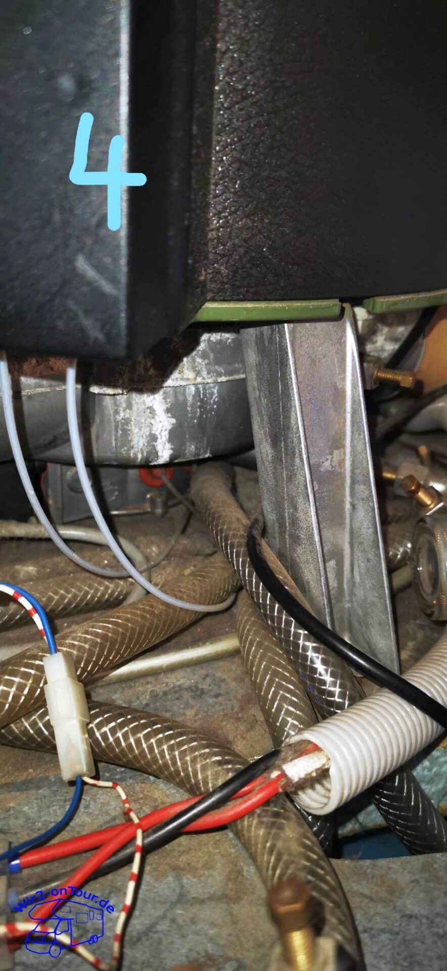 Unterseite des Boilers mit Halteblech, darunter gewebeverstärkte Schläuche, zwei helle Fühlerleitungen und rote und blaue Kabel