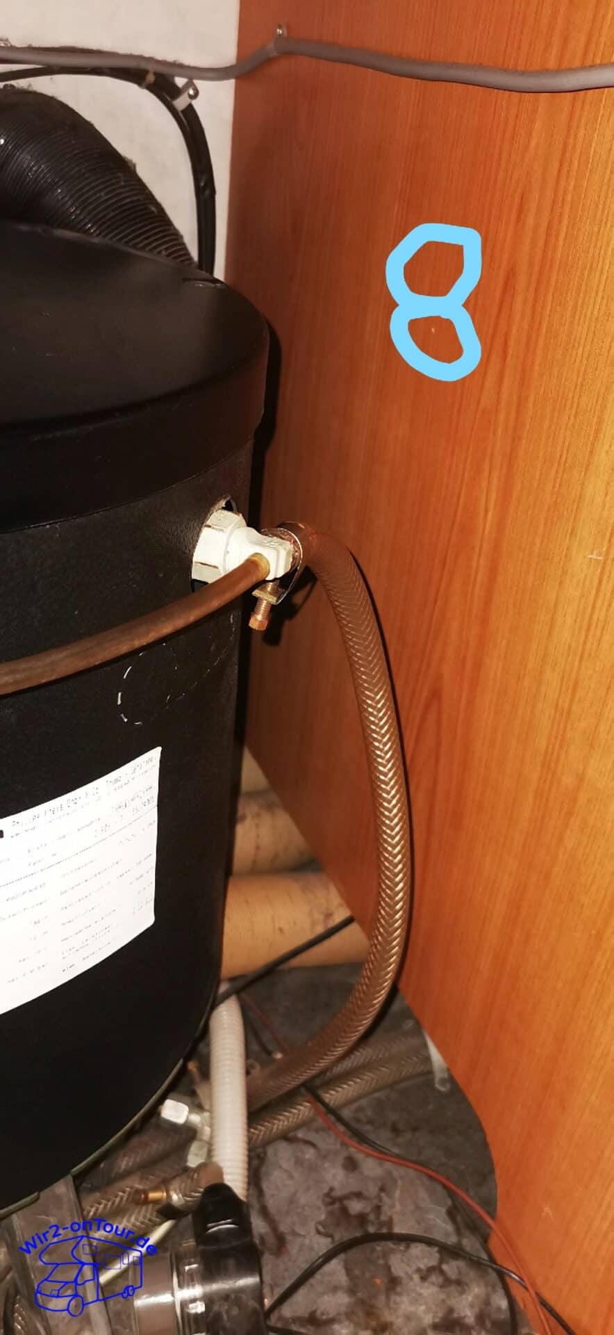 Schwarzer Boiler mit Typenschild im Schrank, seitlich das weiße Entlüftungsventil mit dünnem braunem Schlauch und einem nach unten geführten Wasserschlauch