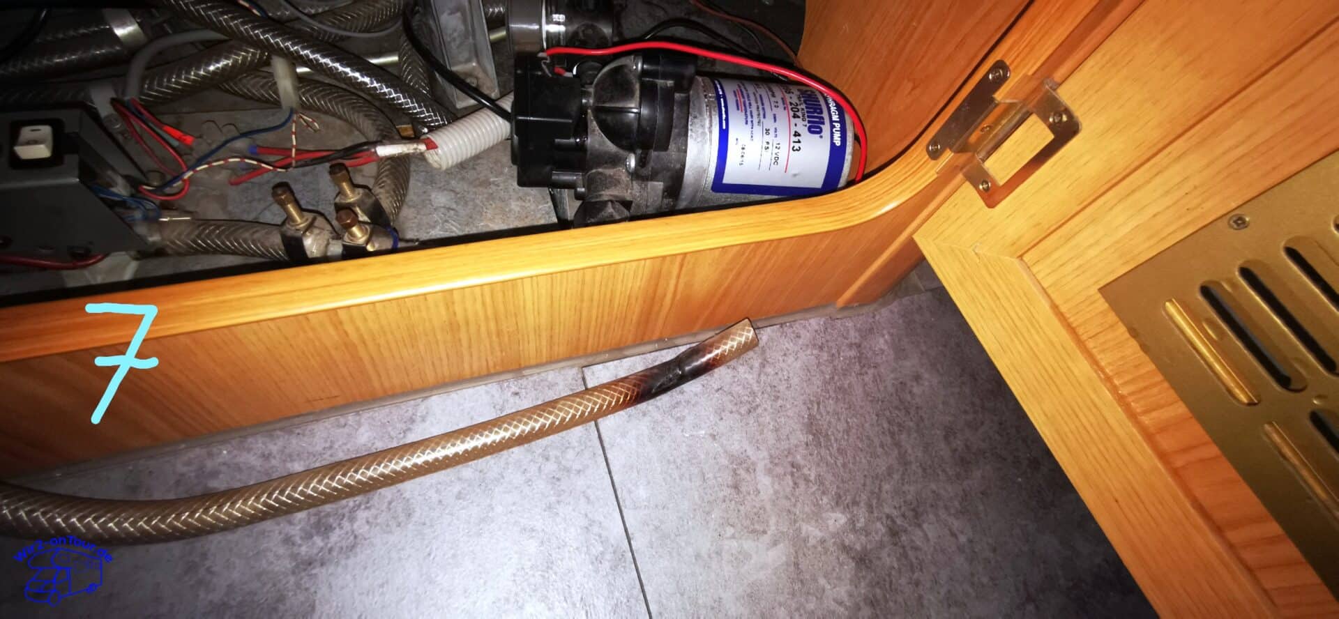 Herausgezogener Schlauch mit verfärbtem Ende liegt auf dem Boden vor dem offenen Staufach mit der Wasserpumpe