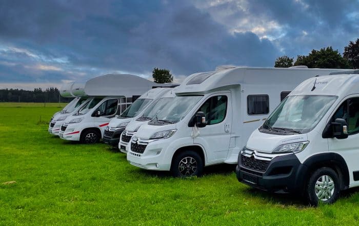 Wohnmobil mit Alkoven und Kastenwagen als Campingfahrzeuge auf einer Wiese
