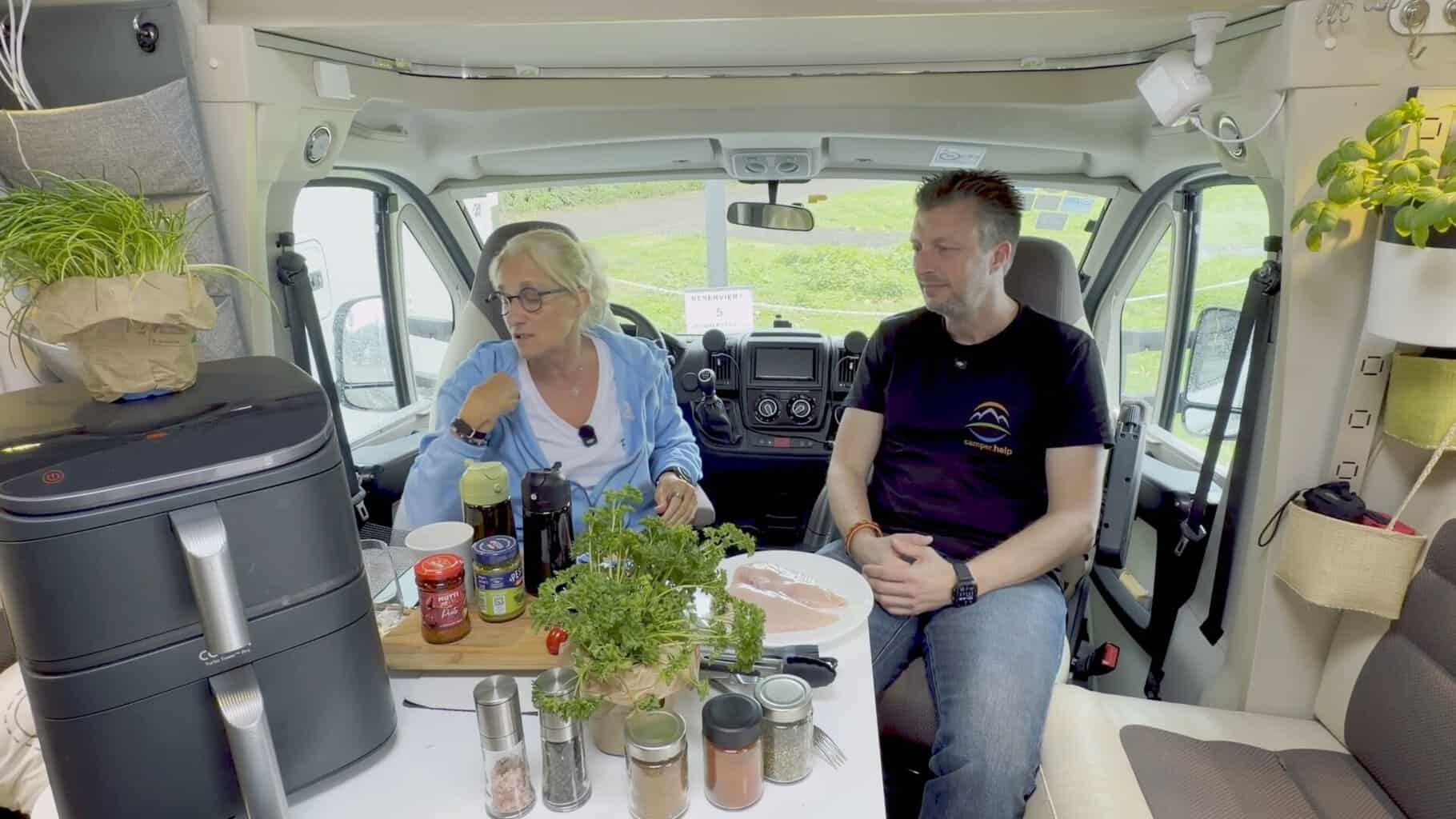anke-und-flo-im-wohnmobil-mit-airfryer Anke und Flo sitzen im Wohnmobil am Tisch, links steht der Airfryer