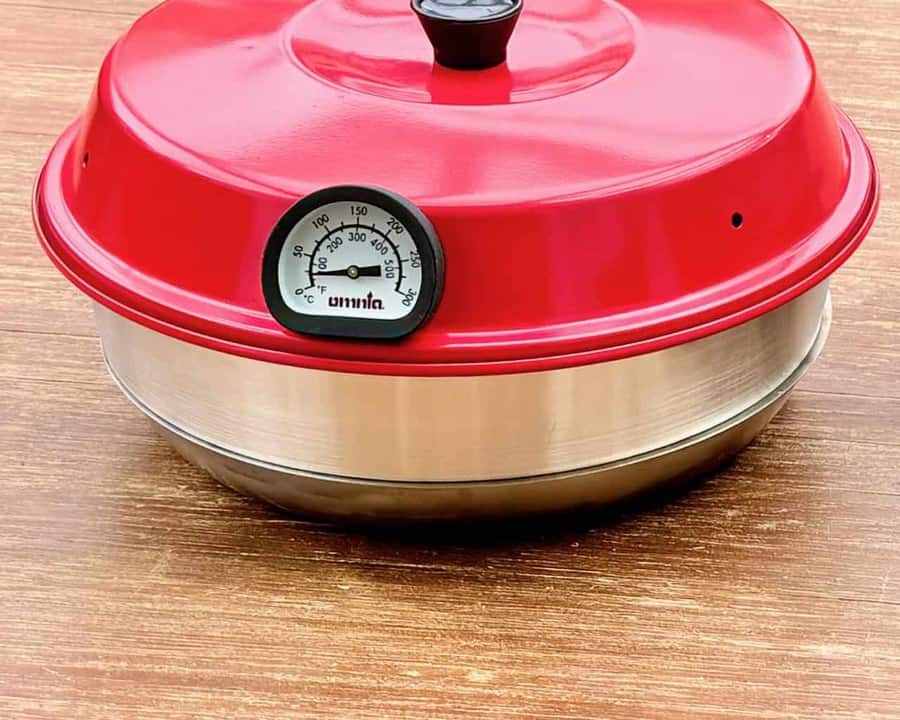 Omnia Camping-Backofen mit rotem Deckel und aufgesetztem Thermometer auf einem Holztisch