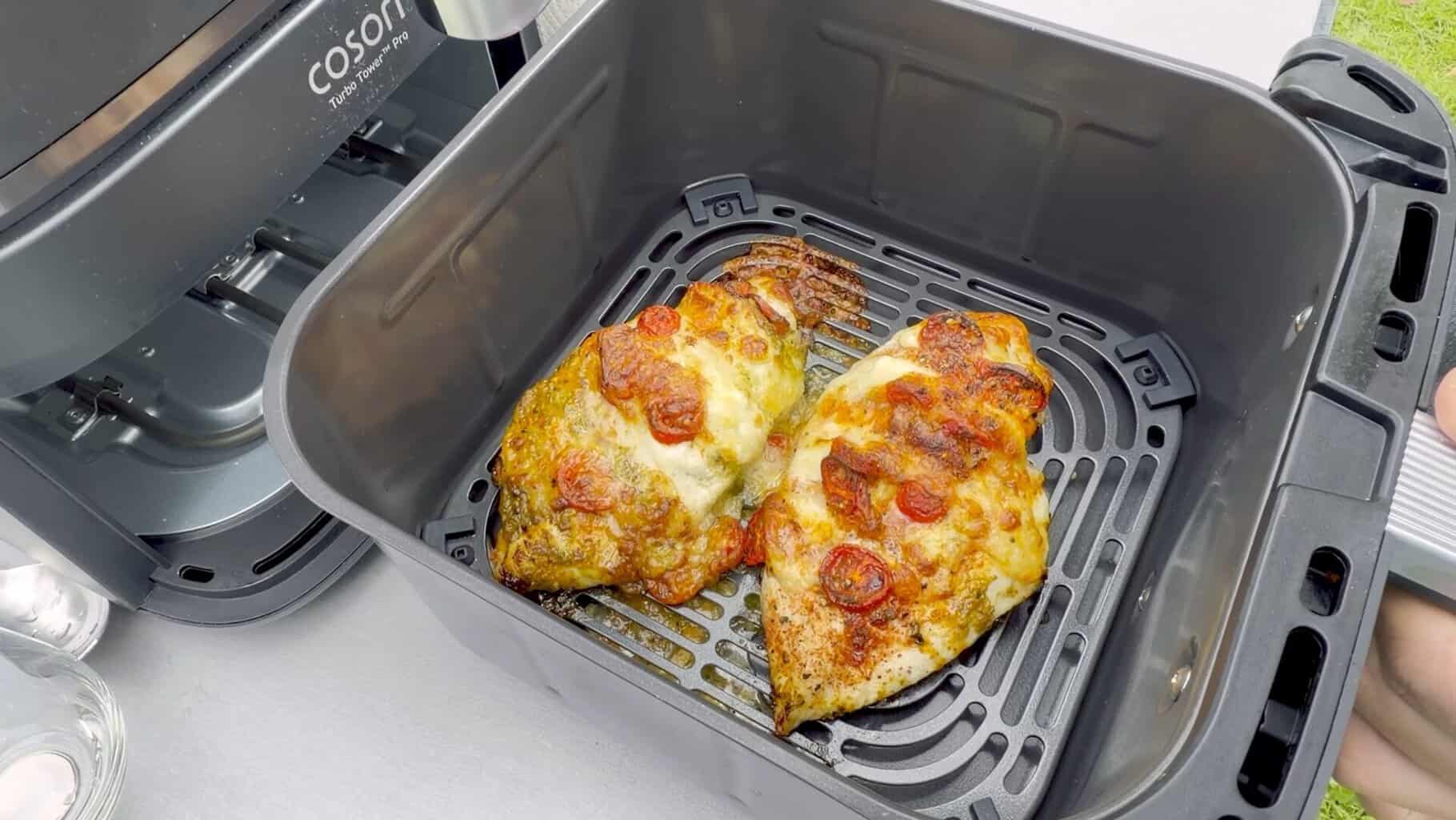 haehnchen-caprese-im-airfryer-korb 2 gefüllte Hähnchenbrüste mit Tomate und Mozzarella im Korb des COSORI Airfryers