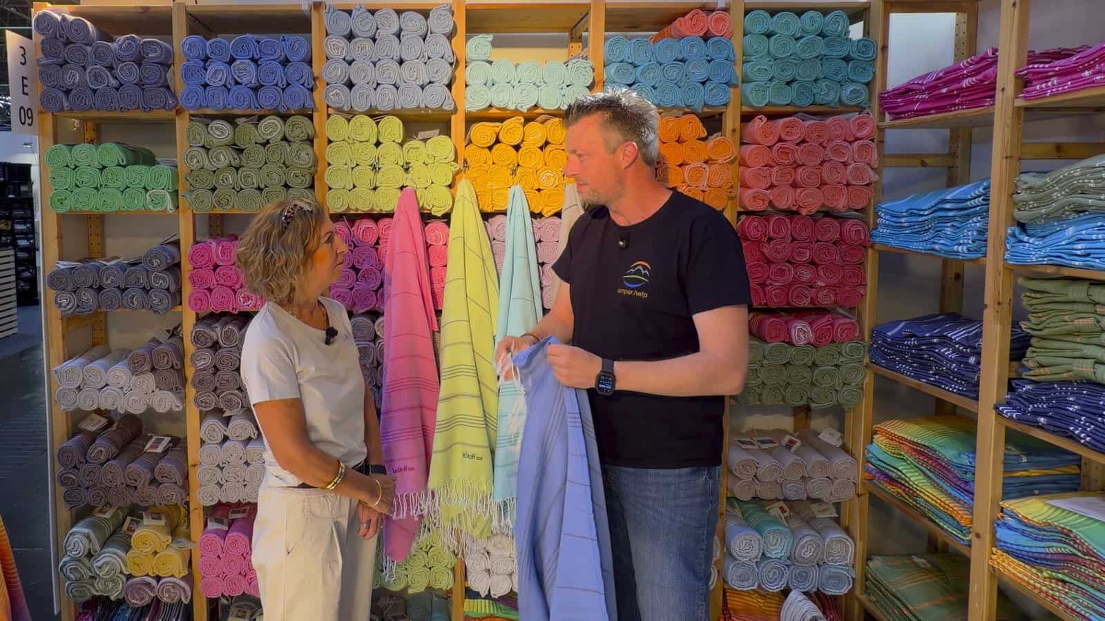 lestoff tuch groessenvergleich Julia von LeStoff und Flo halten am Messestand ein Hamamtuch hoch, dahinter Regale voller bunter Tücher
