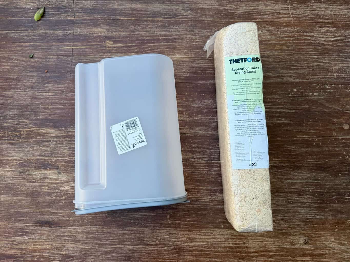 thetford-drying-agent-spender Durchsichtiger Schüttspender neben einer Packung Thetford Separation Toilet Drying Agent auf einem Holztisch